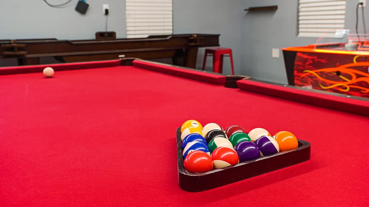 An energetic interior scene with a pool table, colorful billiard balls, an arcade game, and red stools. The space feels fun and inviting, ideal for friendly competitions and game nights among colleagues.