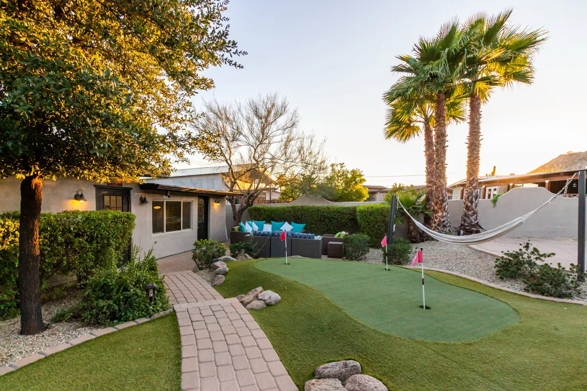 This vibrant image highlights an inviting backyard putting green, a hammock nestled under palm trees, and an adjacent seating area for outdoor gatherings. The lush landscaping and playful amenities evoke both active fun and leisure.