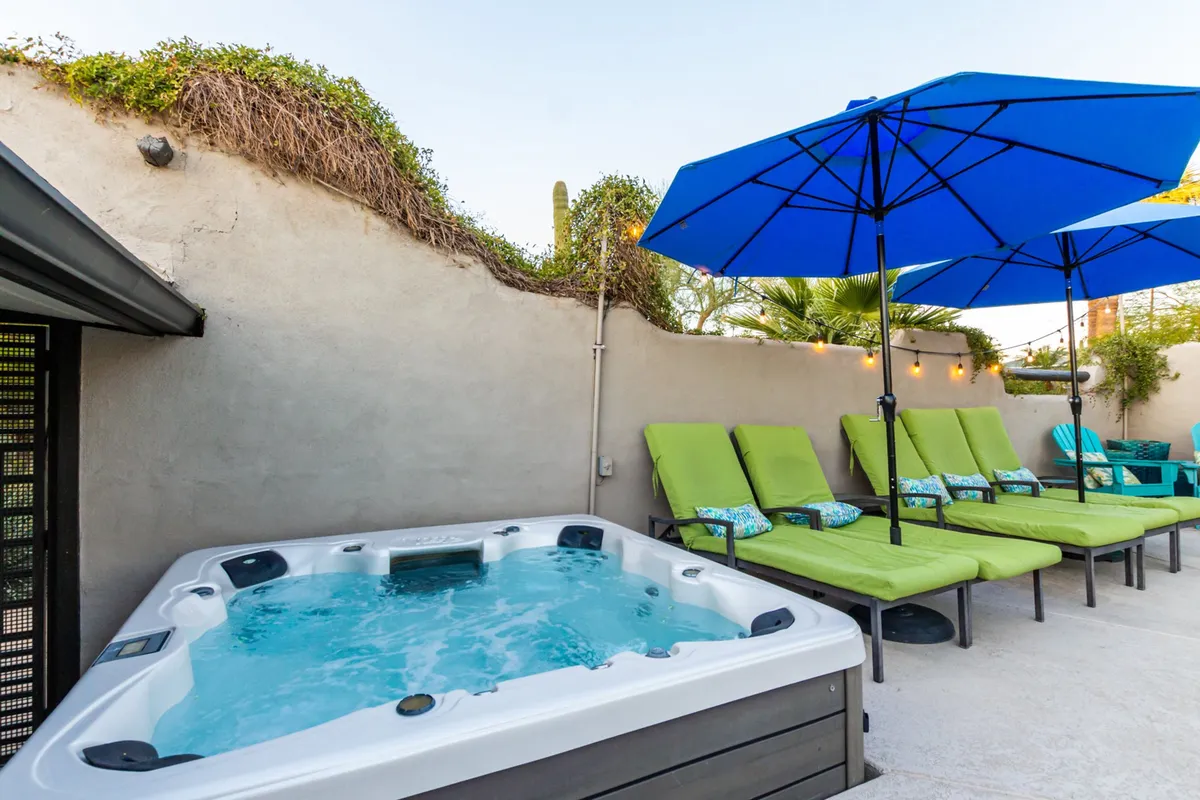 This scene displays a serene outdoor hot tub surrounded by lounge chairs and blue umbrellas, set within a lush backyard. It’s an inviting space for relaxation and recovery, ideal after a day of sports or outdoor fun.