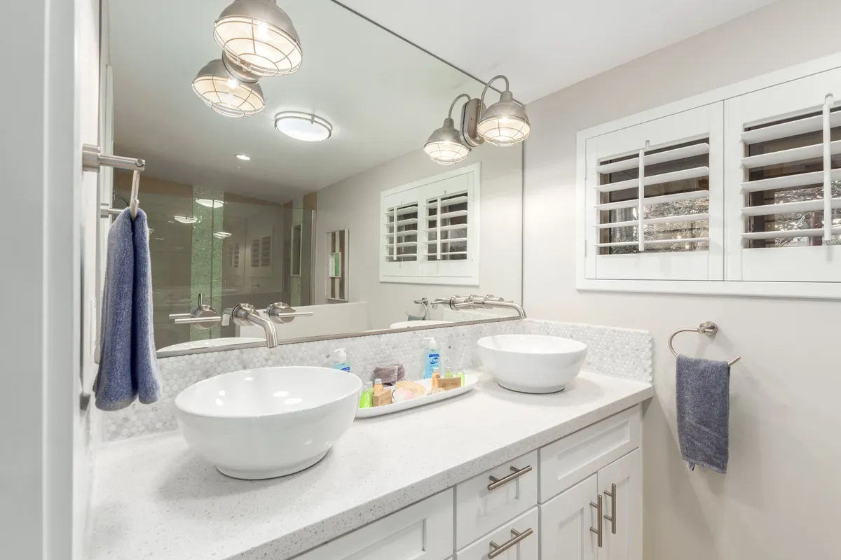 A modern bathroom space with dual vessel sinks, sleek light fixtures, and a large mirror. The room feels clean, spacious, and designed for relaxation—providing an elegant setting for both morning routines and restful evening rituals.