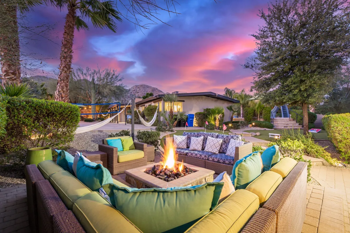 A cozy fire pit scene is surrounded by ample outdoor seating and bordered by hammocks, all set against a beautifully landscaped yard with a mountain view. The fire pit’s gentle glow and the open sky set the mood for s’mores, stargazing, and laughter-filled evenings. The layout encourages group gatherings and relaxed conversation.