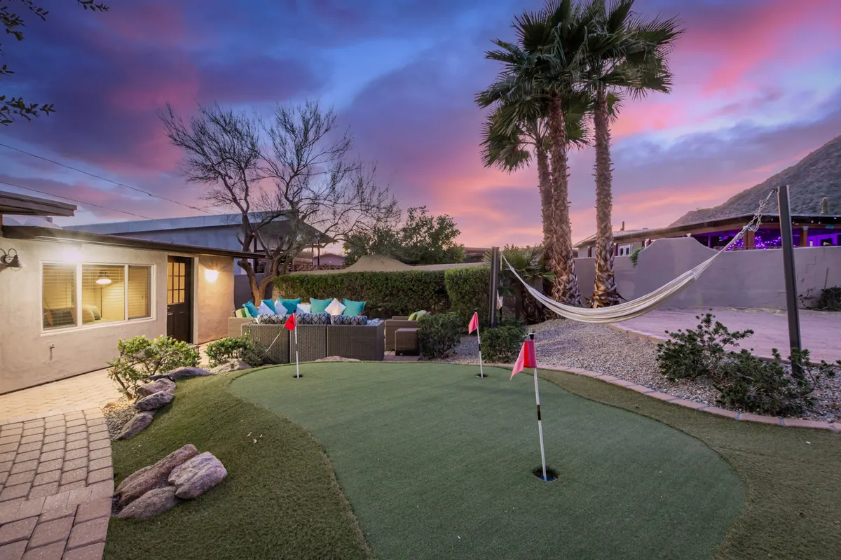 A putting green is featured in this image, flanked by a hammock and palm trees, with a cozy outdoor seating area nearby. The space feels playful and relaxing, ideal for kids and adults alike to unwind or practice their golf.